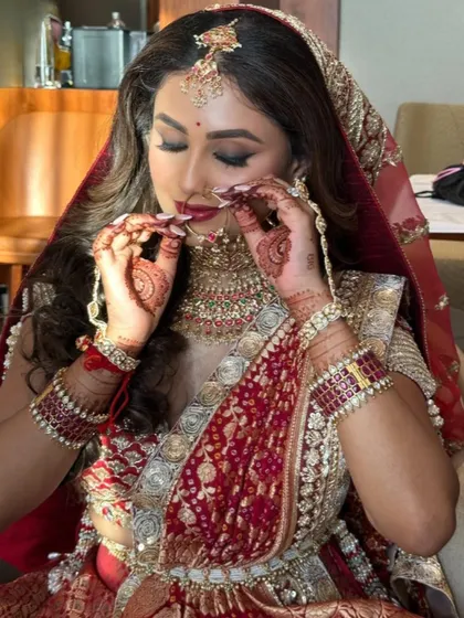 The final touches on a masterpiece. This candid moment captures the intricate details of her jewelry and the flawless finish of her bridal makeup.