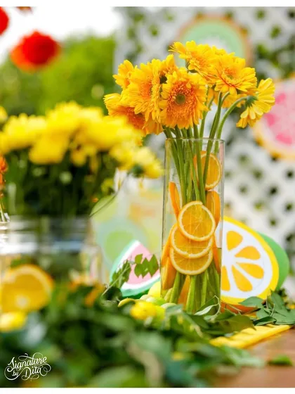 A close-up of a floral centerpiece for a 'Two-tti Fruity' party, with sliced oranges inside the vase for a fresh and colorful detail.