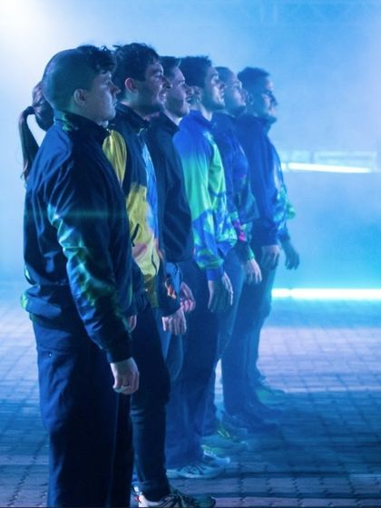 The "To Da Bone" dancers lined up on stage, bathed in blue light. The stark lighting and unified posture create a visually striking and dramatic moment.