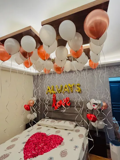 An elegant anniversary decoration with 'Always Love' foil balloons, a heart of rose petals, and a canopy of white and rose gold balloons.