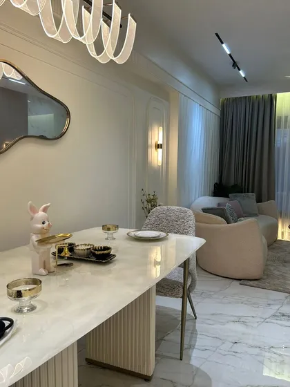 An elegant dining setup featuring a fluted-base marble table and a modern, ribbon-like chandelier. The organic-shaped mirror on the wall adds an artistic touch, reflecting light and making the space feel larger.