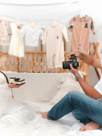 A behind the scenes style shot where the dad to be photographs his partner holding tiny baby shoes. It's a sweet way to capture the anticipation of their new arrival.