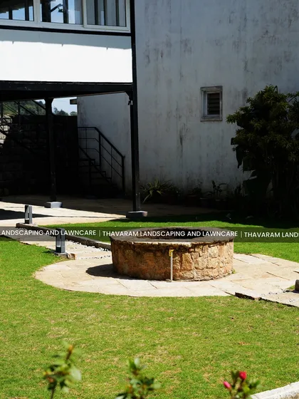A modern home's landscape is softened by the inclusion of a traditional stone well, with subtle outdoor lighting fixtures placed along the path.