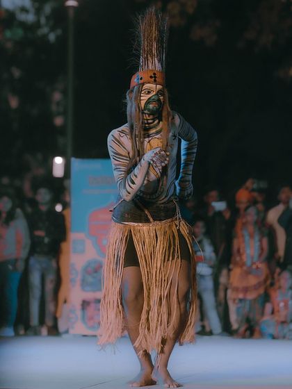 A full-body shot of a tribal dancer in traditional attire, performing for a crowd at Kartavya Path. I aim to capture the full context of the performance, including the artist's costume and stage presence.