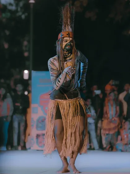 A full-body shot of a tribal dancer in traditional attire, performing for a crowd at Kartavya Path. I aim to capture the full context of the performance, including the artist's costume and stage presence.