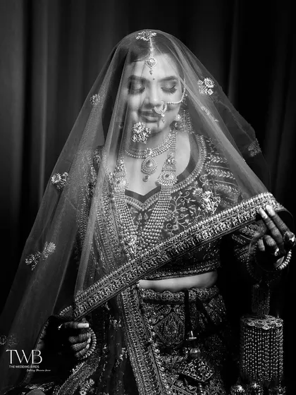 A beautiful black and white portrait of the bride looking down, her face partially covered by her veil. The focus on her intricate jewelry and serene expression creates a classic and elegant feel.