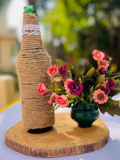 I love creating custom centerpieces. This piece features a jute-wrapped bottle and a small bouquet of artificial flowers on a wooden slice, perfect for a rustic or boho-themed table setting.
