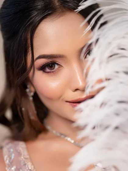 A playful and elegant shot with a white feather. The makeup is glamorous and perfectly executed, highlighting the model's features.
