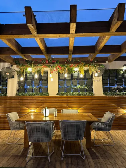 We create stunning gardens even in compact spaces. This terrace dining area is made cozy and intimate with a wooden pergola, hanging lights, and vertical planters.