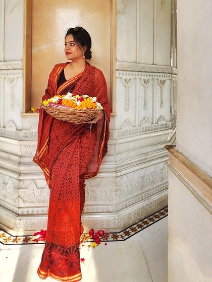 A simple yet elegant red printed saree, perfect for a temple visit or a small puja at home. The look is completed with a basket of fresh flowers.