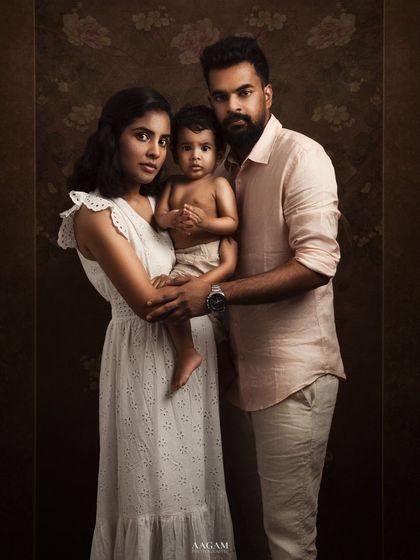 A striking fine art family portrait. The family's coordinated white and neutral outfits against the dark, textured backdrop create a classic and sophisticated look.
