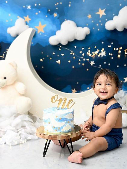 A dreamy cake smash under the stars. This little boy is celebrating his first birthday with a celestial-themed cake on a moon-and-stars backdrop.