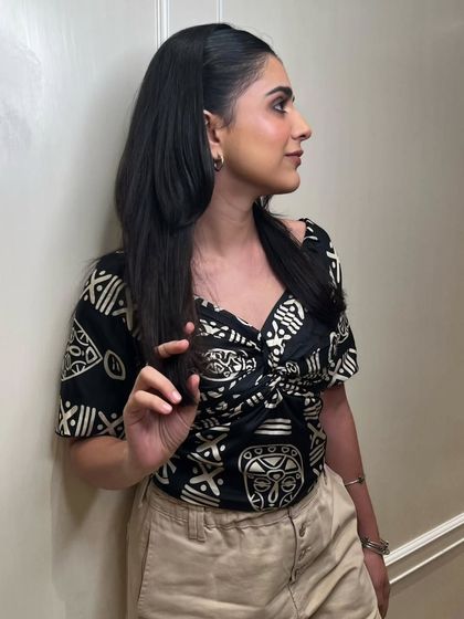 A happy client showcasing her finished look. The makeup is a warm, neutral palette with a focus on glowing skin and softly defined features, paired with a simple yet chic half-up hairstyle.