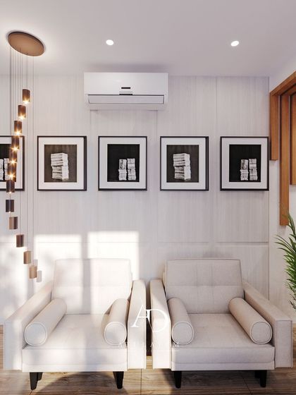A minimalist seating area with two white armchairs, a cascading pendant light, and a series of framed black and white art prints.