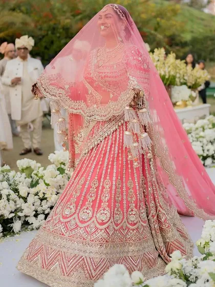 A stunning shot of the bride in her gorgeous pink lehenga, smiling as she walks through the floral-lined aisle.