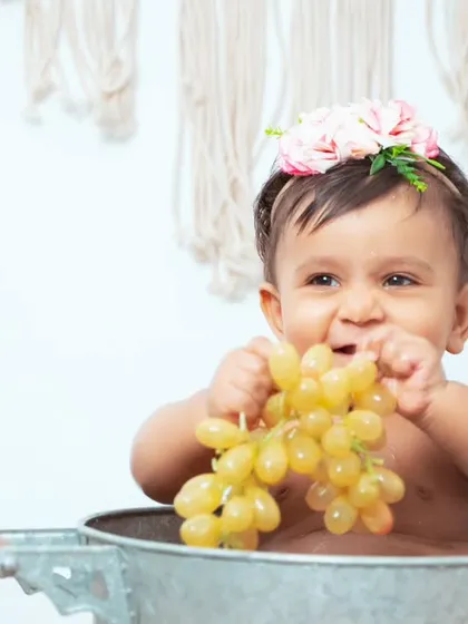 A baby enjoys a healthy snack of grapes during a rustic-themed bath session. We love incorporating fun and safe elements for them to interact with.
