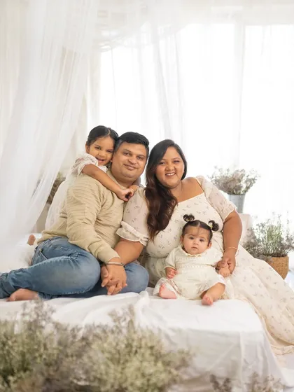 A happy family of four posing on a bed in a light-filled studio. This cozy, lifestyle setup is perfect for capturing natural family connections.