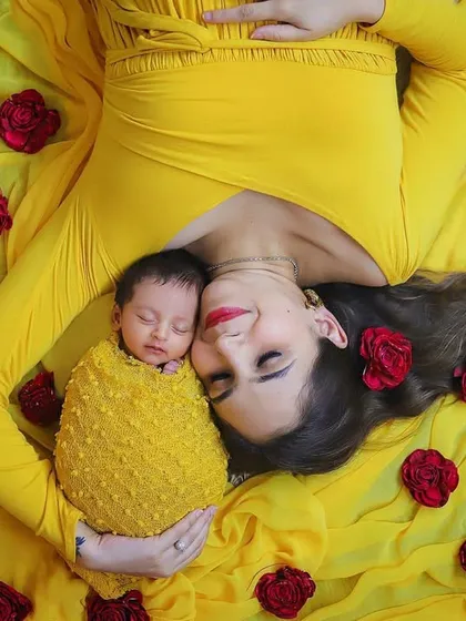 A bright and cheerful portrait of a mother and her newborn. Lying on a bed of yellow fabric with red roses, this image is full of color and happiness, perfectly capturing the joy of a new baby.