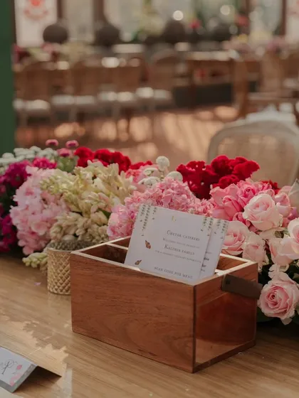 A custom wooden box for guest messages, surrounded by a lush arrangement of pink and red flowers. I love creating interactive and personalized elements for guests.