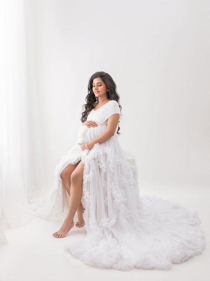 Seated by the window, the natural light illuminates her beautifully. The white ruffled gown looks angelic in this high-key lighting setup.