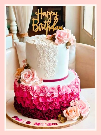 A stunning two-tier cake with ombre ruffles in shades of pink and burgundy, topped with delicate sugar roses.