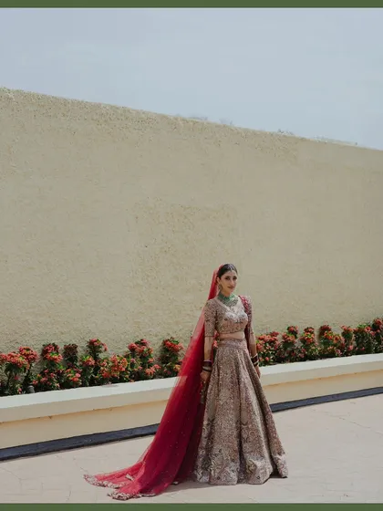 A full-length portrait of the bride in her stunning Anita Dongre lehenga with a long, flowing red veil. The simple background allows her regal attire to take center stage.