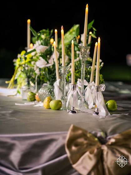A close-up of a candlelit centerpiece, with a large gold bow on the draped table linen adding a touch of glamour.