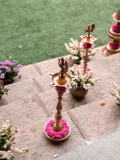 Traditional brass lamps (diyas) decorated with flowers, placed on the stone steps, add a warm, auspicious glow to the ceremony.