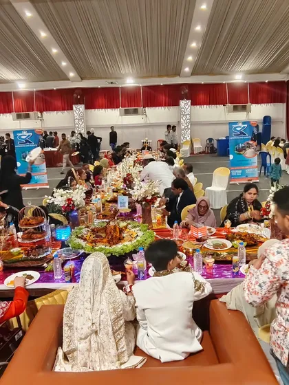 A wide shot of a grand wedding feast, with the bride and groom seated at the head of a long, lavishly decorated table.