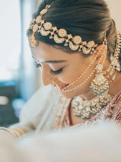 A candid moment of bridal elegance. Her side profile highlights the intricate matha patti and the soft, blended contouring that defines her features without looking heavy, perfect for a modern bride.