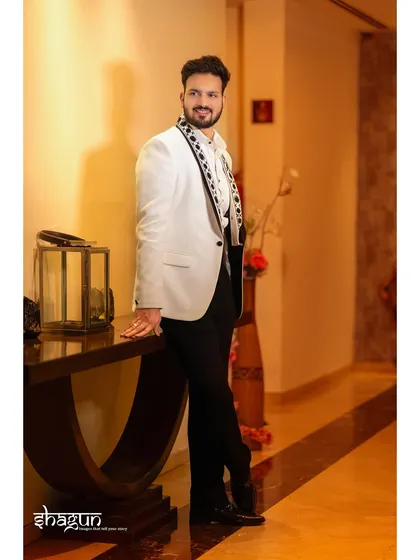 A full-length portrait of the groom, looking dapper in his white jacket. The hotel corridor provides a sophisticated backdrop.