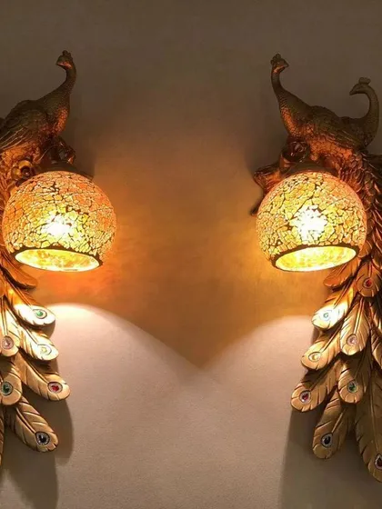Inspired by India's national bird, these peacock wall lights bring a touch of regal artistry to your home. The detailed golden feathers and cracked glass globe create a warm, inviting glow that is both dramatic and elegant.