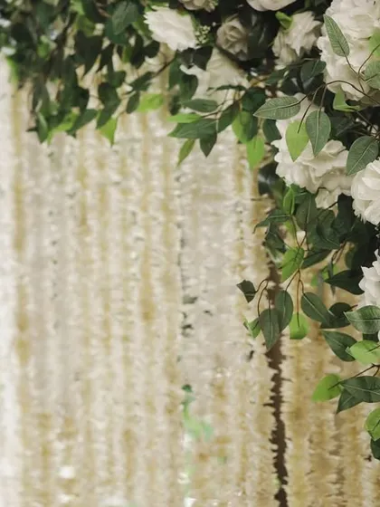 A close-up of the floral arch, focusing on the texture of the white roses and the curtain of hanging jasmine flowers behind it. We believe in layering elements to create depth and beauty.