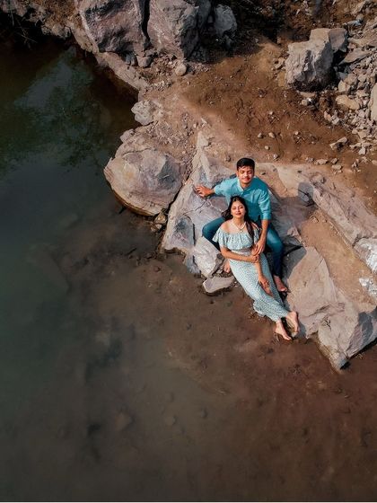 An aerial drone shot of a couple relaxing by a rocky shore. This perspective offers a unique and grand view of their connection with the landscape.