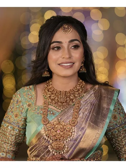 A portrait of elegance. This bride's soft glam makeup, with its subtle shimmer on the eyes and glowing skin, is the perfect complement to her traditional temple jewelry and silk saree.