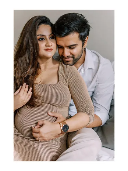 A classic, loving pose that beautifully showcases the baby bump. The soft lighting and neutral tones keep the focus entirely on the couple's gentle embrace and shared excitement.
