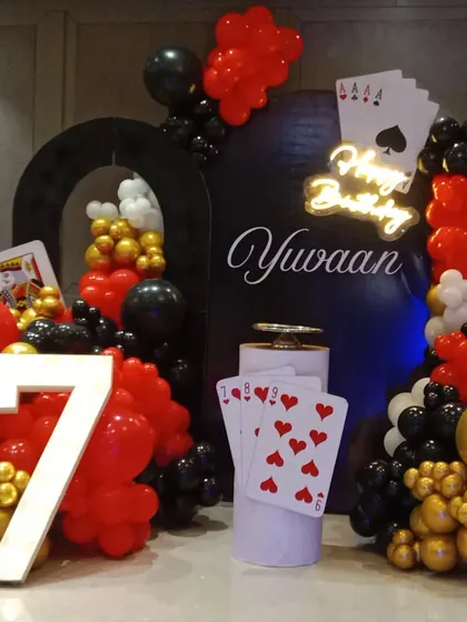 A fun casino and cards theme for a 7th birthday. I used red, black, and gold balloons, large playing card props, a 'Happy Birthday' neon sign, and a light-up number '7'.