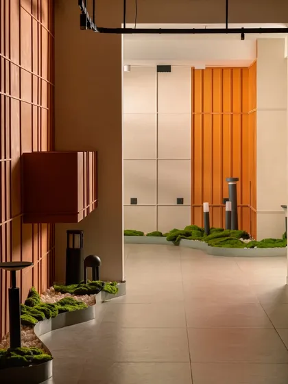 This angle showcases the layered design, with the terracotta grid wall in the foreground and the bright orange paneling in the distance. The outdoor lighting fixtures are displayed naturally along the moss bed.