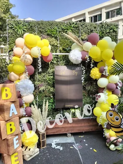 A full view of an outdoor "What will it Bee?" gender reveal party. I used a green wall as a natural backdrop, adding wooden 'BABEE' blocks, a cute bee cutout, and a balloon garland in yellow, maroon, and beige.