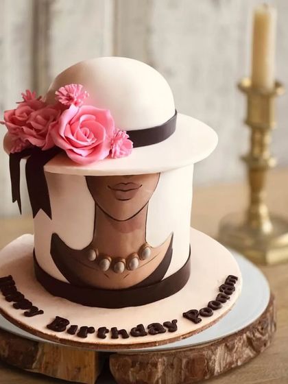 An artistic and stylish cake designed to look like a vintage hat box, with a hand-painted face and pink sugar roses.