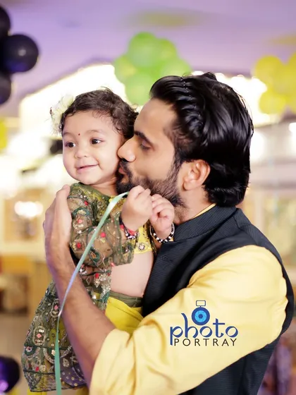 A tender moment between father and daughter, as he gives her a kiss on the cheek during her first birthday party.