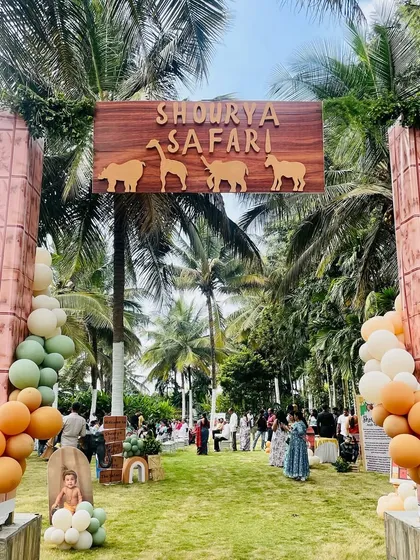 A stylish and modern entrance for Shourya's safari party. The setup features a wooden sign with animal silhouettes, set between two pillars and framed by organic balloon arches in muted orange, green, and white tones.