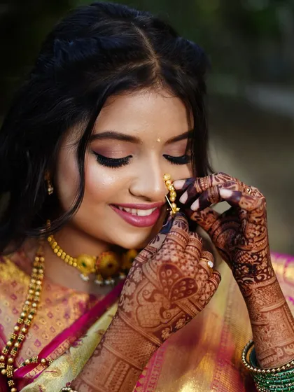 A beautiful close-up of a Maharashtrian bride adjusting her nath. The focus is on her glowing skin, kohl-rimmed eyes, and the intricate henna.