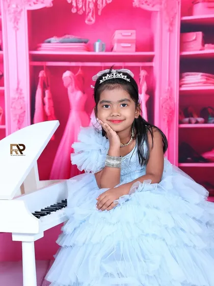 For your growing princess, I design elegant and playful portraits. Here, a young girl in a beautiful blue gown poses by a miniature white piano against a stylish pink closet backdrop, capturing her charming personality.