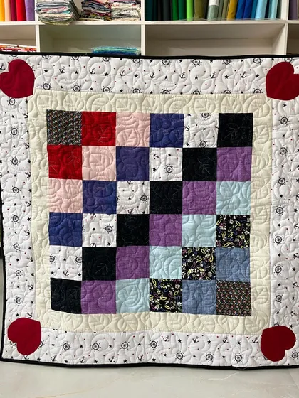 This assorted baby quilt combines various fabric squares in a checkerboard pattern, finished with charming heart appliqués in the corners.