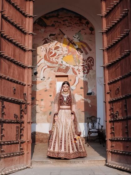 A powerful portrait of a bride standing in the entrance of a grand wooden door at Neemrana Fort.