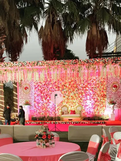 Planning a grand shadi? We design breathtaking wedding stages like this one, featuring a massive wall of pink and white flowers, elegant seating for the couple, and professional lighting to create a romantic, picture-perfect setting.