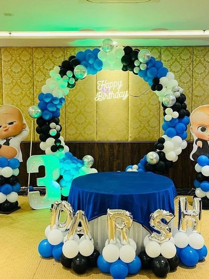 A Boss Baby themed cake-cutting stage with a circular balloon arch and character cutouts.