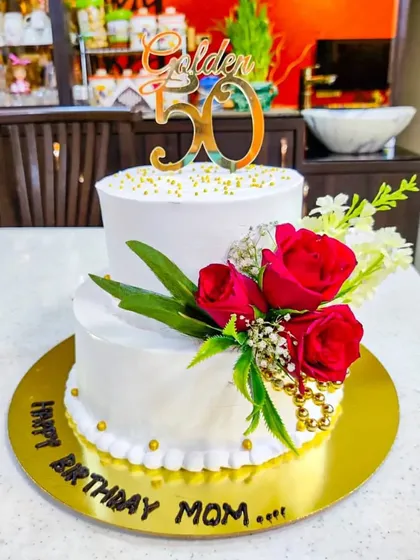A beautiful two-tier cake for a mom's golden 50th birthday. The simple white design is elevated by a cascade of fresh red roses, creating a look of timeless elegance.