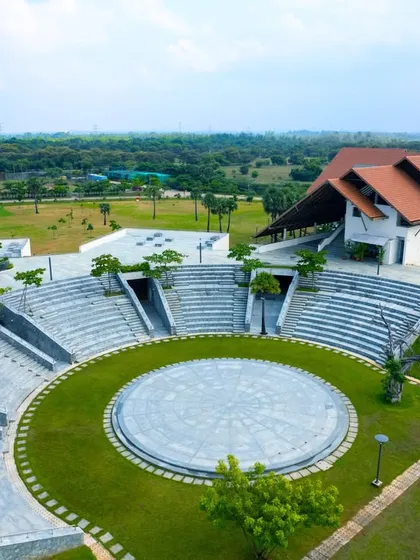 An aerial view of the large, open-air amphitheater at Vellore International School in Chennai. This space serves as the heart of the campus, a central node for school gatherings that is seamlessly integrated with the surrounding green landscape and waterbodies.